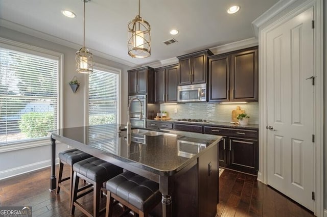 kitchen featuring a kitchen island with sink, decorative light fixtures, crown molding, and appliances with stainless steel finishes