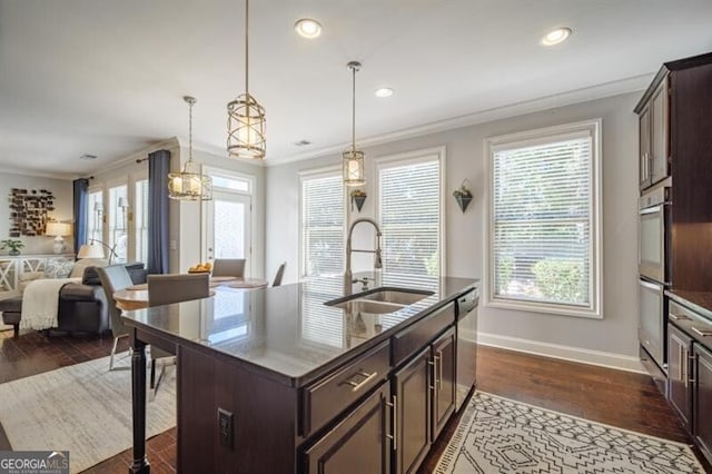 kitchen with dark brown cabinetry, sink, decorative light fixtures, ornamental molding, and an island with sink