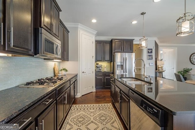 kitchen with stainless steel appliances, sink, hanging light fixtures, and a center island with sink