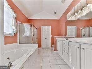 bathroom with vanity, tile patterned flooring, vaulted ceiling, and plus walk in shower