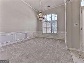 unfurnished dining area featuring ornamental molding, light carpet, and a chandelier