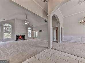 unfurnished living room with light carpet, ceiling fan with notable chandelier, vaulted ceiling, and a large fireplace