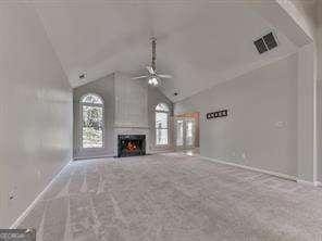 unfurnished living room featuring carpet floors, lofted ceiling, a large fireplace, and ceiling fan