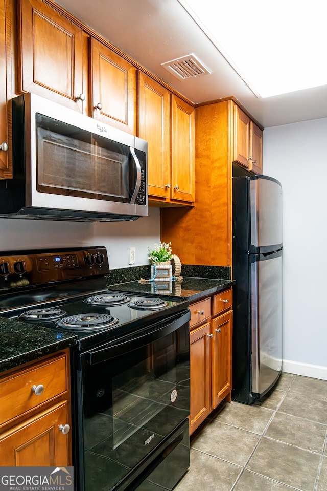 kitchen with stainless steel appliances, light tile patterned floors, and dark stone countertops