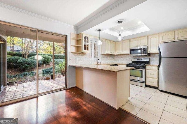 kitchen featuring appliances with stainless steel finishes, hanging light fixtures, kitchen peninsula, a raised ceiling, and light stone countertops