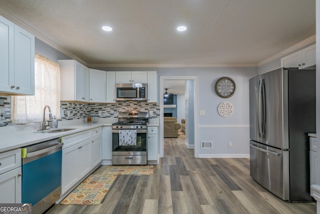 kitchen featuring sink, white cabinetry, stainless steel appliances, ornamental molding, and light wood-type flooring