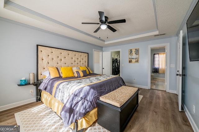 bedroom with dark hardwood / wood-style floors, a walk in closet, a tray ceiling, crown molding, and a closet