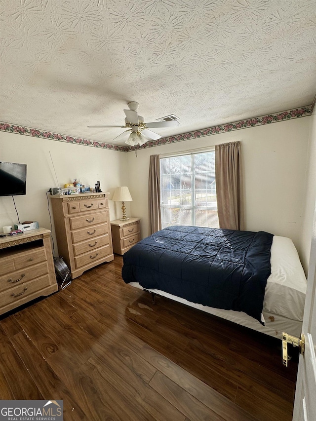 bedroom with ceiling fan, a textured ceiling, and dark hardwood / wood-style flooring