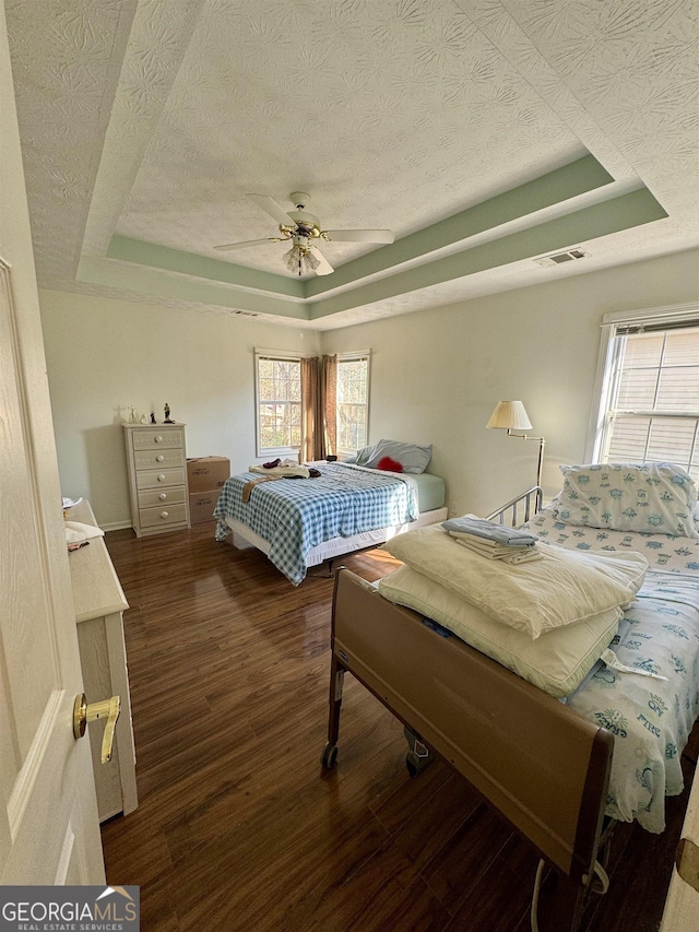 bedroom with multiple windows, a textured ceiling, ceiling fan, and a tray ceiling