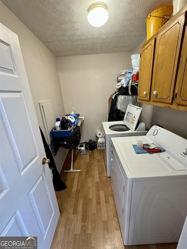 laundry room with a textured ceiling, cabinets, washing machine and clothes dryer, and light wood-type flooring