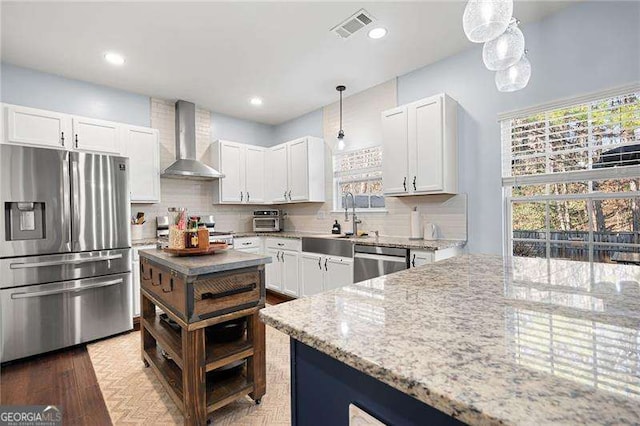 kitchen with appliances with stainless steel finishes, pendant lighting, white cabinets, and wall chimney exhaust hood