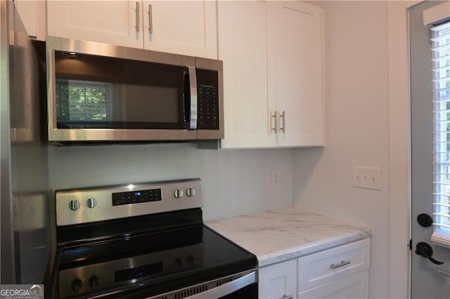 kitchen with stainless steel appliances, white cabinetry, and light stone counters