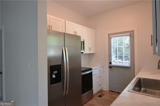 kitchen featuring white cabinetry, sink, stainless steel appliances, light stone countertops, and light wood-type flooring