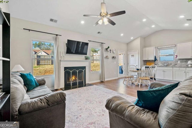 living room with hardwood / wood-style floors, vaulted ceiling, sink, and a wealth of natural light