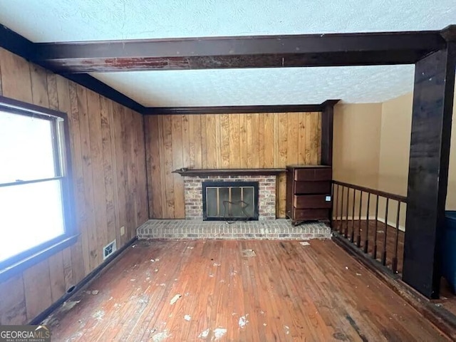 unfurnished living room featuring beamed ceiling, hardwood / wood-style floors, a fireplace, and wood walls