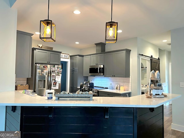 kitchen with gray cabinets, appliances with stainless steel finishes, decorative light fixtures, kitchen peninsula, and a barn door