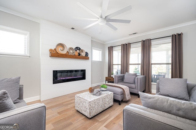 living room featuring ceiling fan, ornamental molding, a large fireplace, and light hardwood / wood-style floors