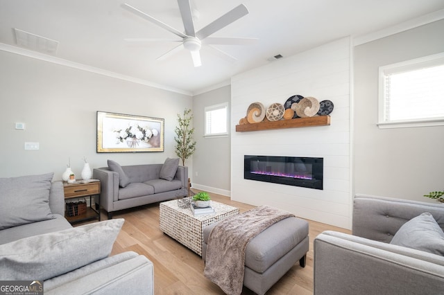 living room featuring crown molding, light hardwood / wood-style floors, a large fireplace, and ceiling fan