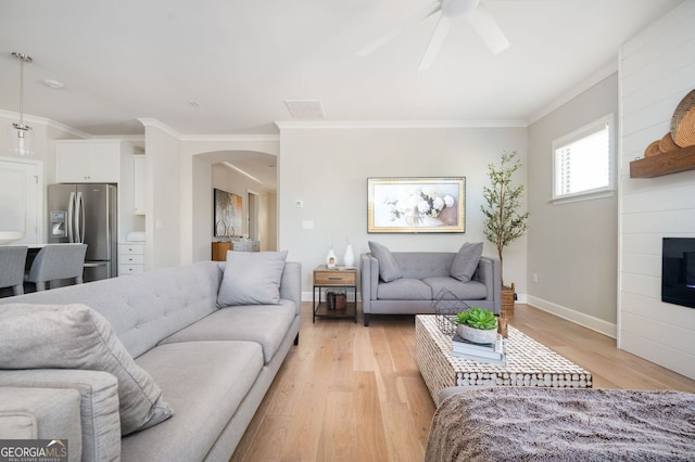 living room with ceiling fan, arched walkways, light wood finished floors, a fireplace, and baseboards