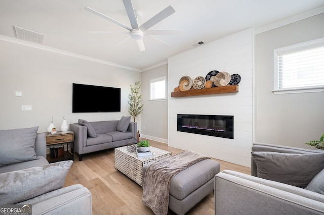 living area featuring light wood-type flooring, visible vents, a large fireplace, and ceiling fan