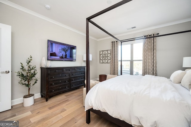 bedroom featuring light wood finished floors, baseboards, visible vents, and ornamental molding