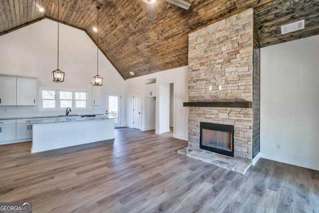 kitchen featuring a stone fireplace, hardwood / wood-style floors, pendant lighting, high vaulted ceiling, and white cabinets