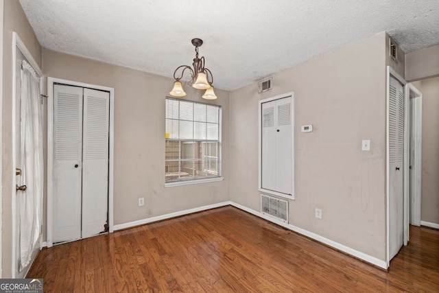 unfurnished bedroom featuring hardwood / wood-style flooring, an inviting chandelier, a textured ceiling, and two closets