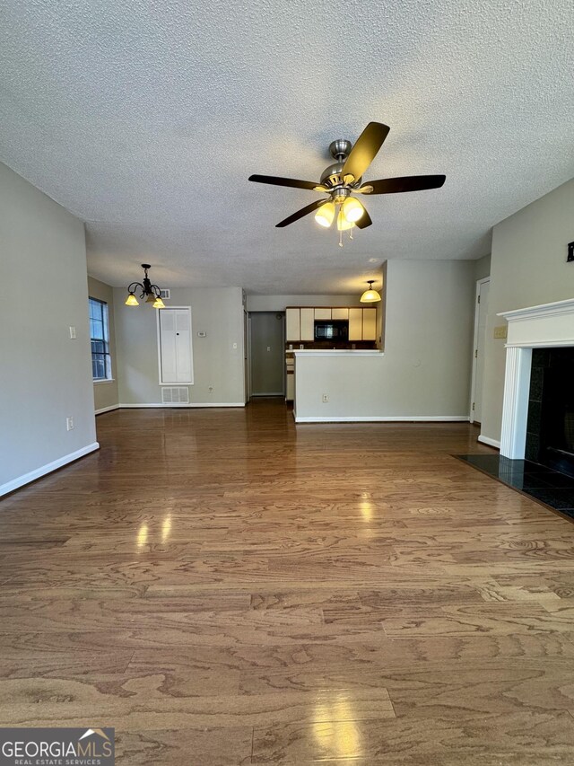 unfurnished living room with wood-type flooring, ceiling fan with notable chandelier, and a textured ceiling