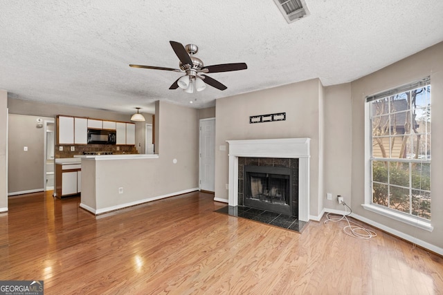 unfurnished living room with ceiling fan, a fireplace, a textured ceiling, and light wood-type flooring