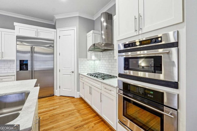 kitchen featuring appliances with stainless steel finishes, backsplash, light stone counters, white cabinets, and wall chimney exhaust hood