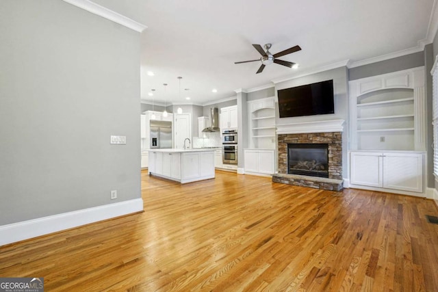 unfurnished living room with sink, crown molding, light wood-type flooring, ceiling fan, and a fireplace