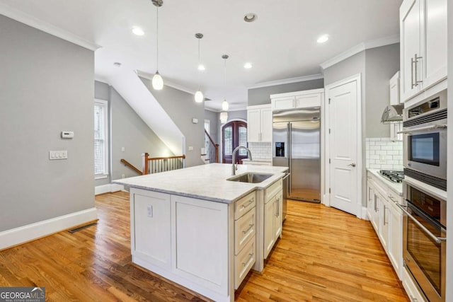 kitchen with sink, appliances with stainless steel finishes, an island with sink, pendant lighting, and backsplash