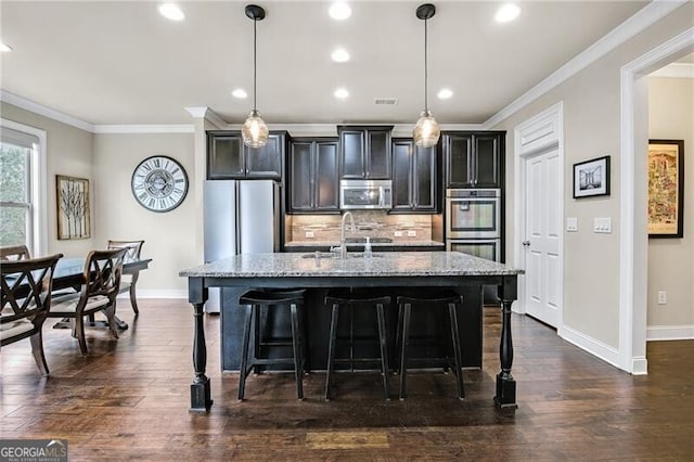 kitchen with pendant lighting, sink, backsplash, stainless steel appliances, and a center island with sink