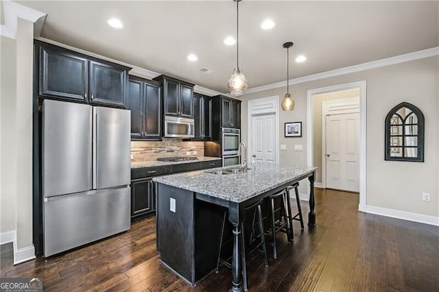 kitchen with a breakfast bar, light stone counters, decorative light fixtures, an island with sink, and stainless steel appliances