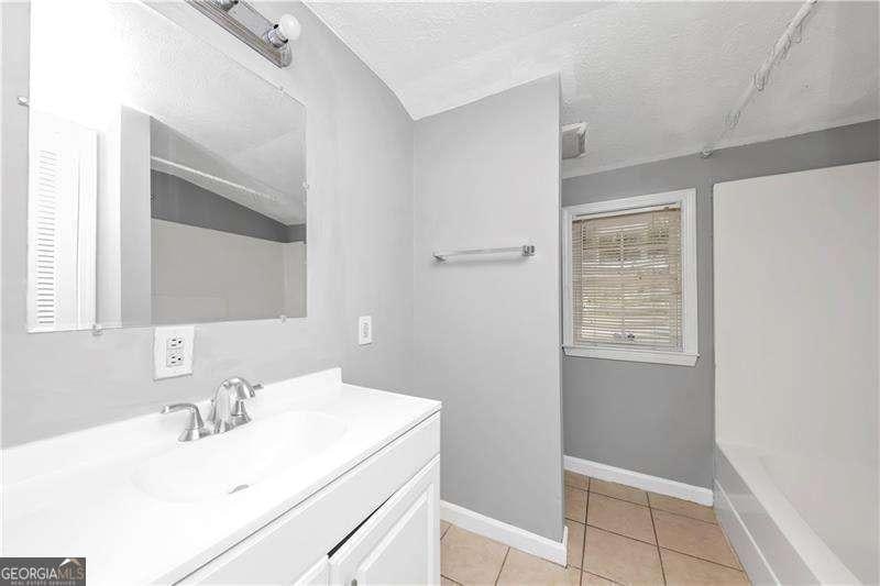 bathroom featuring lofted ceiling, vanity, walk in shower, tile patterned floors, and a textured ceiling