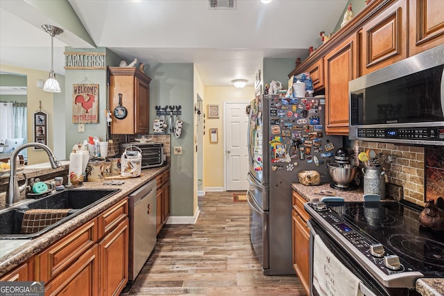 kitchen with sink, decorative light fixtures, light hardwood / wood-style flooring, appliances with stainless steel finishes, and decorative backsplash