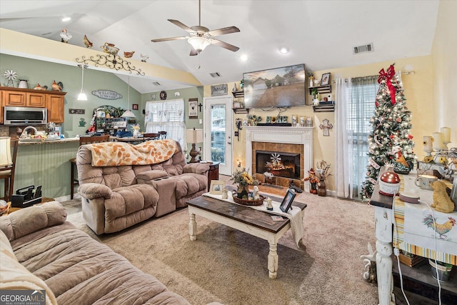 carpeted living room featuring ceiling fan, a healthy amount of sunlight, a tiled fireplace, and high vaulted ceiling