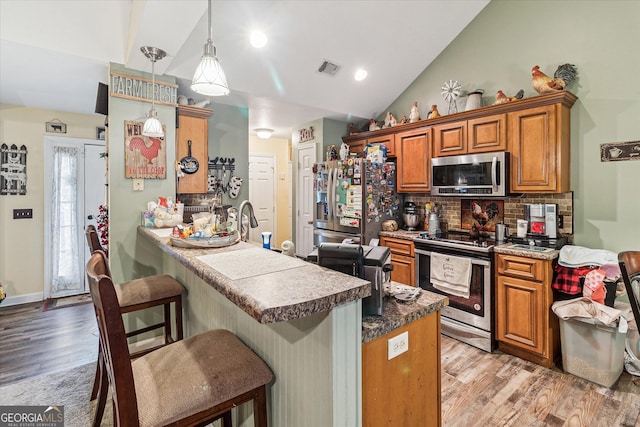 kitchen with pendant lighting, lofted ceiling, decorative backsplash, kitchen peninsula, and stainless steel appliances