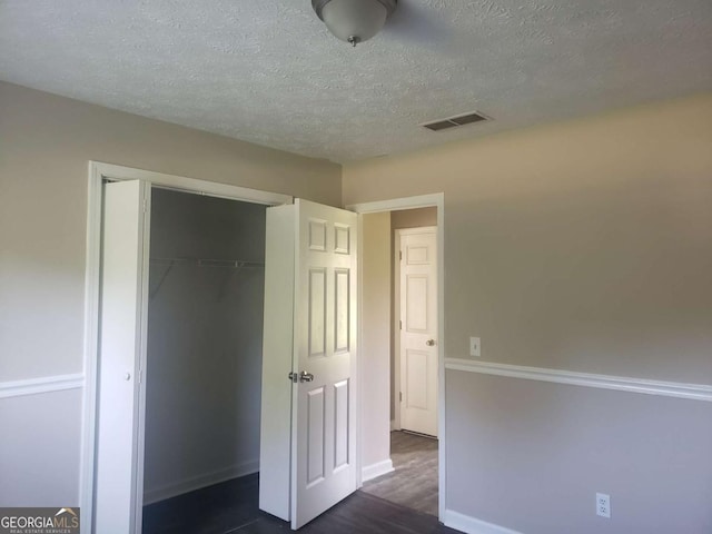 unfurnished bedroom featuring dark wood-type flooring, a closet, and a textured ceiling