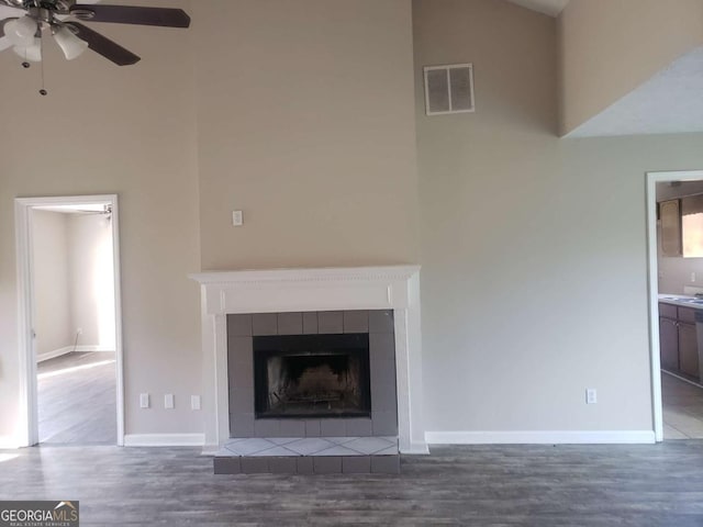 unfurnished living room featuring a tile fireplace, dark hardwood / wood-style floors, and ceiling fan