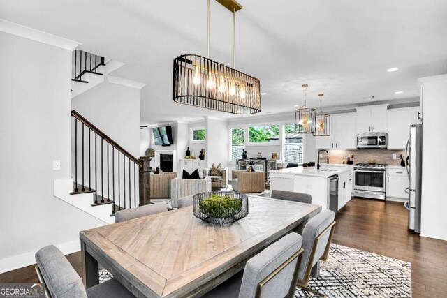 dining area featuring an inviting chandelier, sink, crown molding, and dark hardwood / wood-style floors