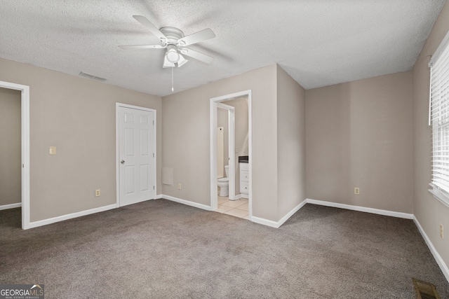 unfurnished bedroom with ensuite bathroom, light carpet, a textured ceiling, and ceiling fan