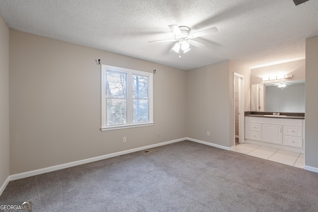 unfurnished bedroom with connected bathroom, sink, ceiling fan, light carpet, and a textured ceiling