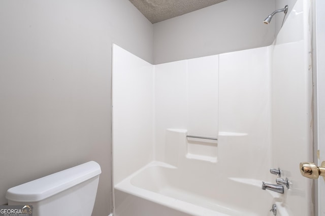 bathroom with a textured ceiling, shower / bathtub combination, and toilet