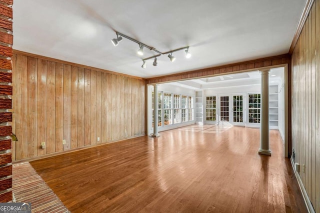 interior space with rail lighting, wood walls, hardwood / wood-style flooring, and ornate columns