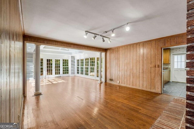 unfurnished living room with plenty of natural light, wooden walls, decorative columns, and hardwood / wood-style floors