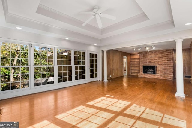 unfurnished living room featuring a raised ceiling, a fireplace, and decorative columns