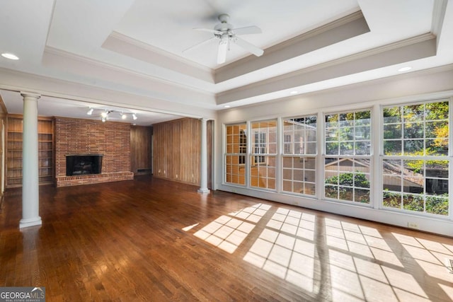 unfurnished living room with a brick fireplace, ornamental molding, decorative columns, and a raised ceiling