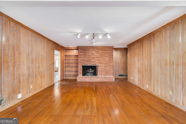 unfurnished living room with built in features, a fireplace, wood walls, rail lighting, and hardwood / wood-style flooring