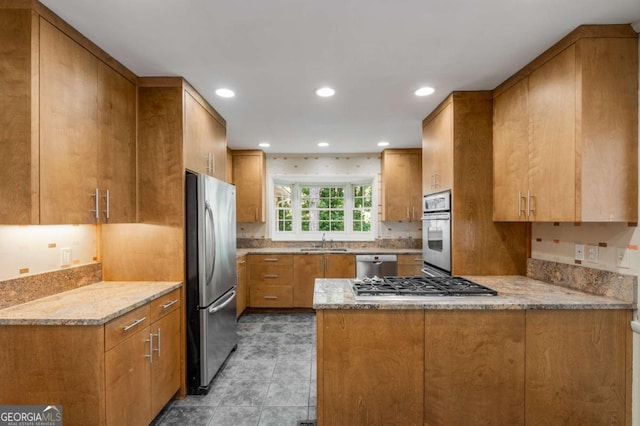 kitchen with sink, light stone countertops, kitchen peninsula, and appliances with stainless steel finishes